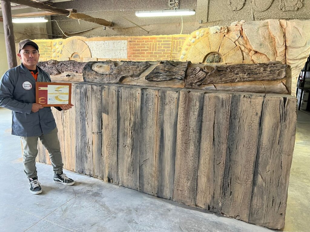 Alumno del curso de tematización de madera y troncos con diploma de aplicador tematizador Estecha delante de mostrador de tablones envejecidos reproducidos con mortero